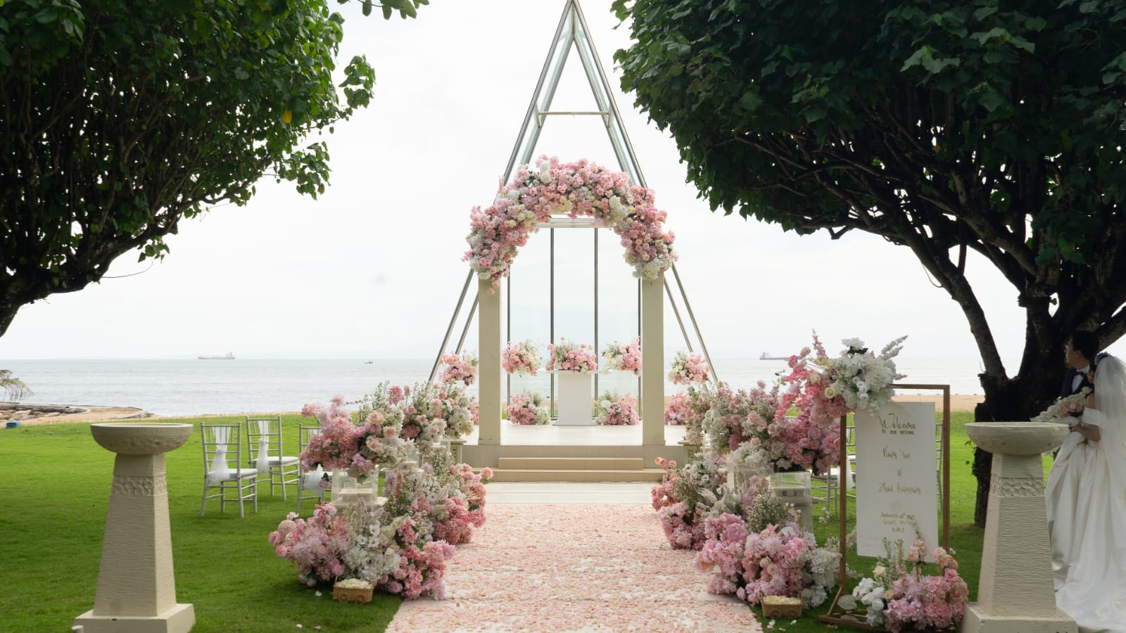 Blush floral arch on a coastal wedding chapel with a petal-lined aisle